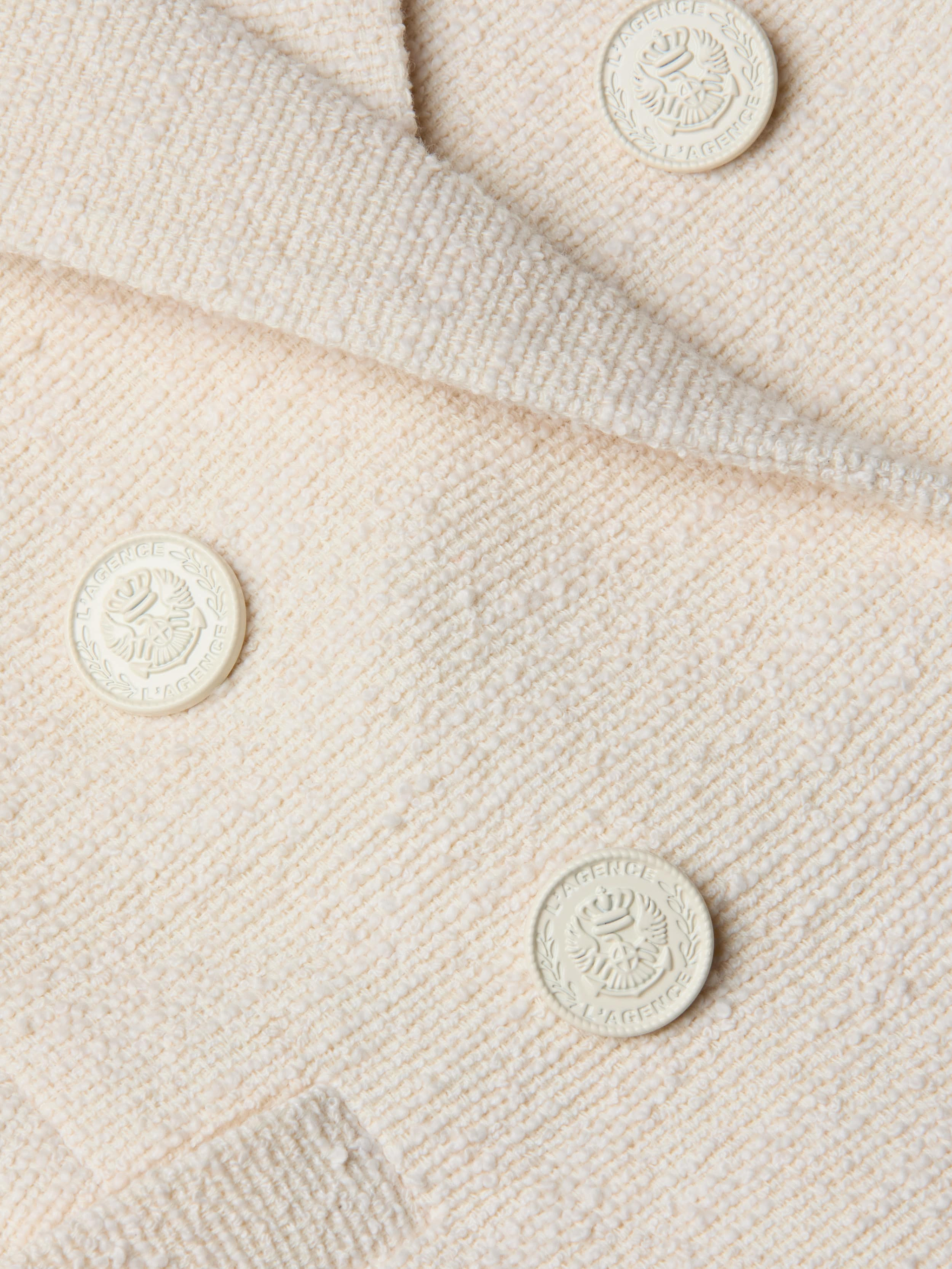 Close-up of the cream-colored, textured fabric from the Brooke Tweed Blazer, showcasing four embossed round buttons adorned with a laurel wreath and crest design.