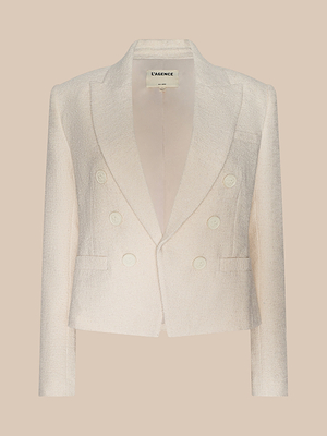 The Brooke Tweed Blazer is an elegant, cream-colored double-breasted blazer with four buttons and a notched lapel, showcased against a plain beige background.