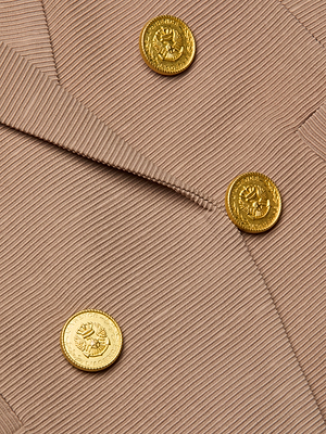 Close-up of the Brooke Blazer in light brown, made from lightweight ribbed fabric. Features sharp lapels, neat stitching, overlapping edges, and three shiny gold embossed buttons on a double-breasted front.