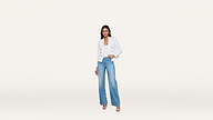Woman wearing a white blazer with gold buttons, blue wide-leg jeans, and white heels, standing against a plain white background.