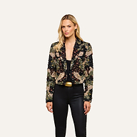 A woman wearing the Jen Crystal Blazer—a couture-inspired, hand-embellished piece—over a black top and pants stands against a plain, light background, looking at the camera with a neutral expression.