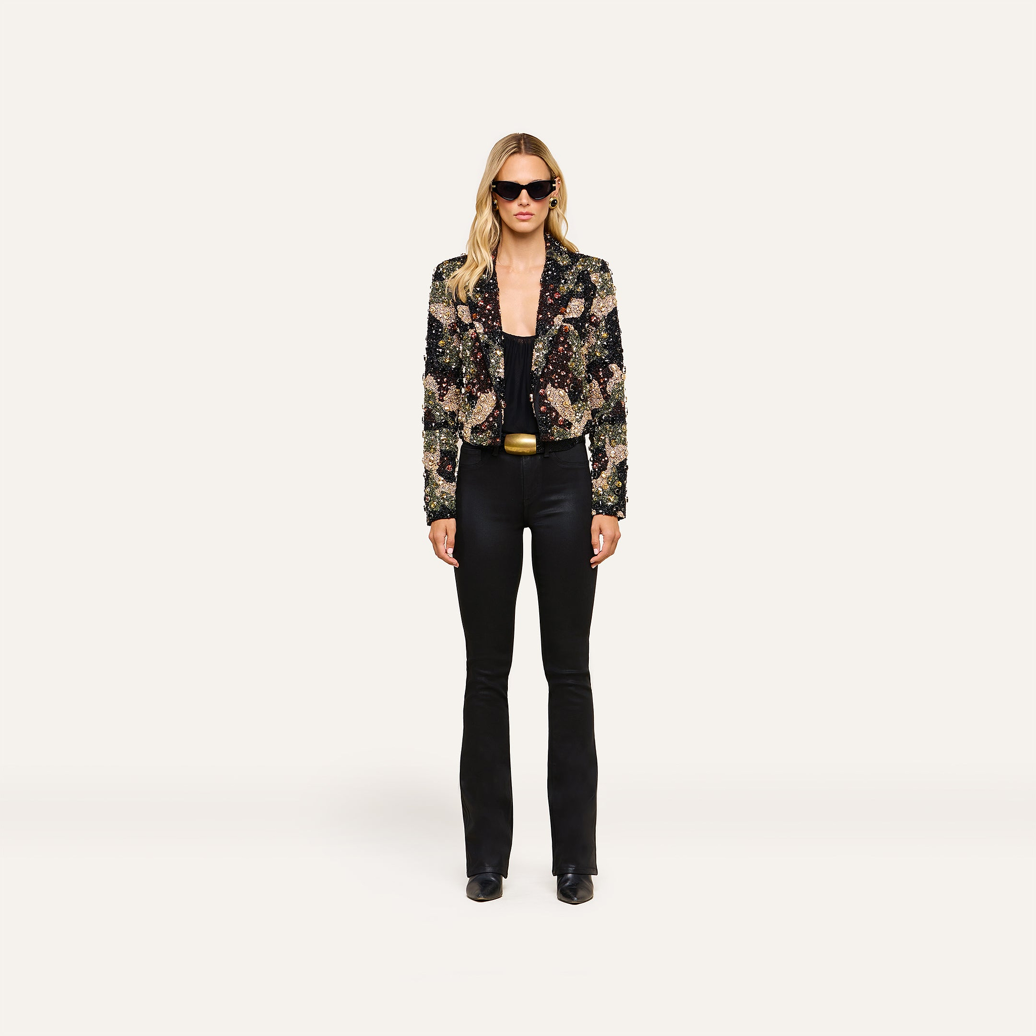 Woman wearing black sunglasses, the Jen Crystal Blazer—a couture-inspired, hand-embellished piece—paired with a black top, black flared pants, and black shoes stands against a plain white background.