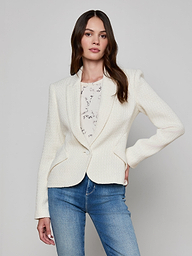 A woman models the Jennah Tweed Blazer in ivory, styled over a light patterned blouse and blue jeans. She stands against a plain light background with one hand on her hip.