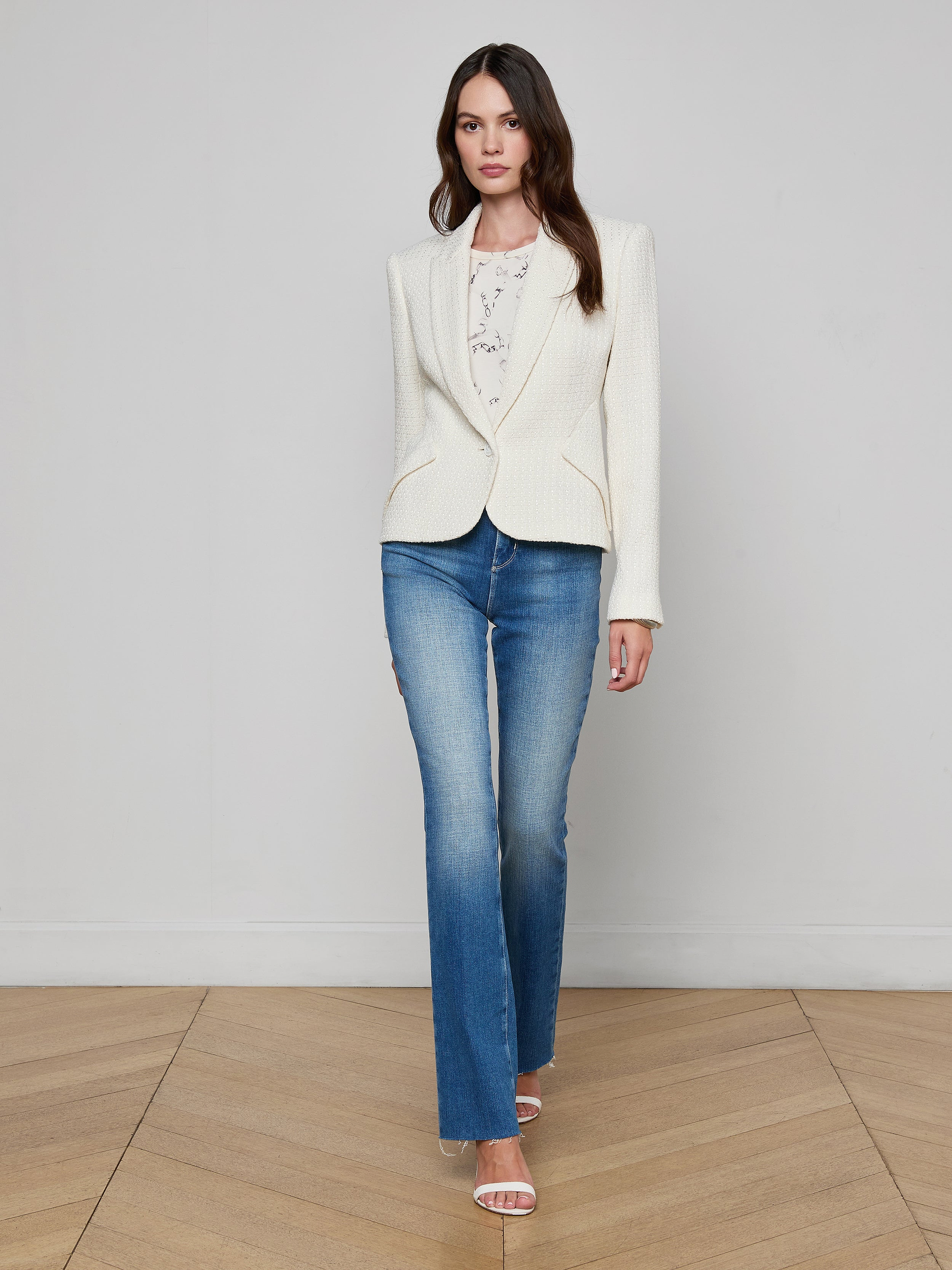 A woman wearing the Jennah Tweed Blazer, a printed blouse, blue jeans, and heels stands against a plain white background, looking straight ahead with a neutral expression.