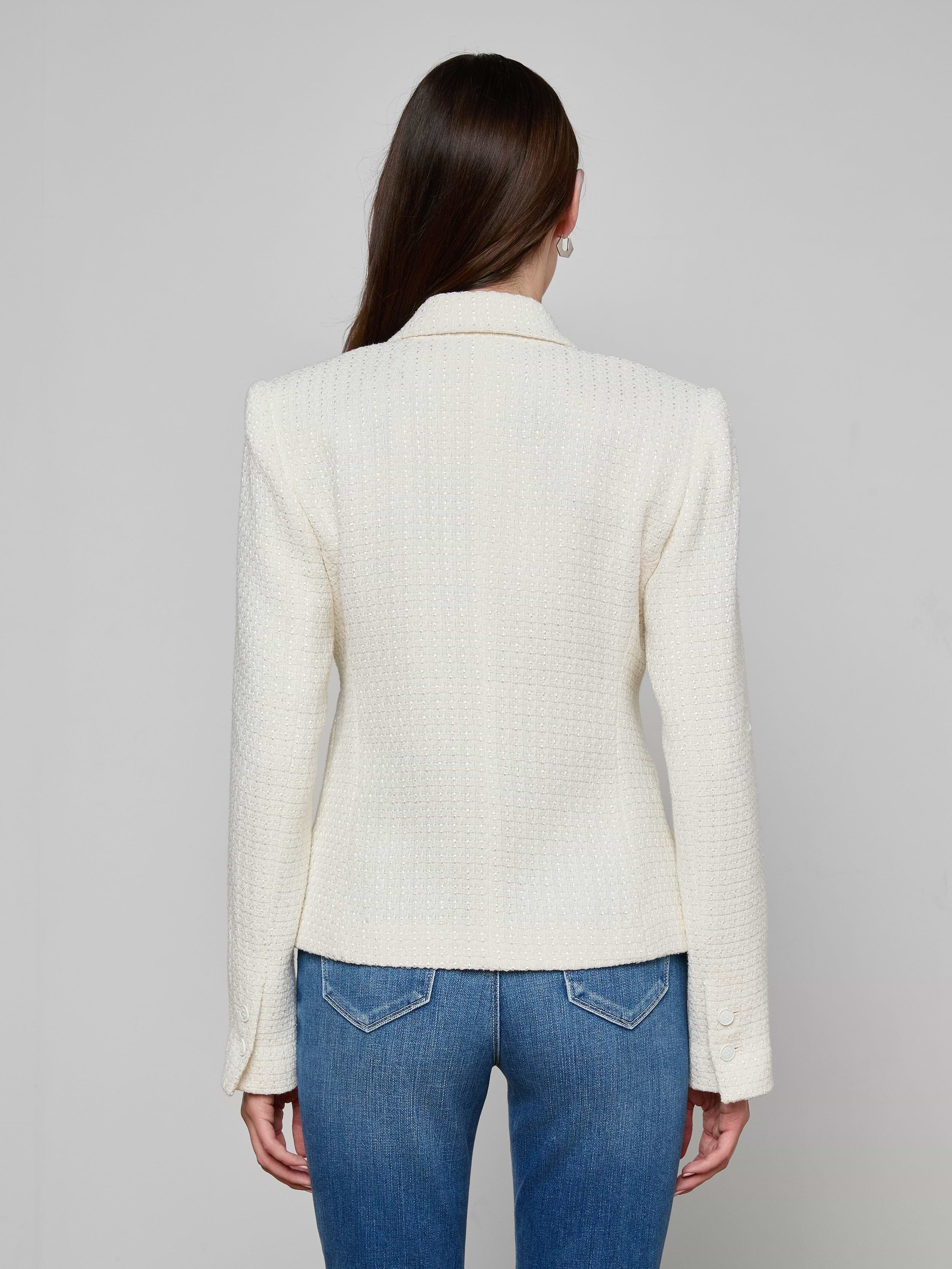 A woman with long brown hair faces away, wearing the petite Jennah Tweed Blazer in ivory and blue jeans against a plain light background.