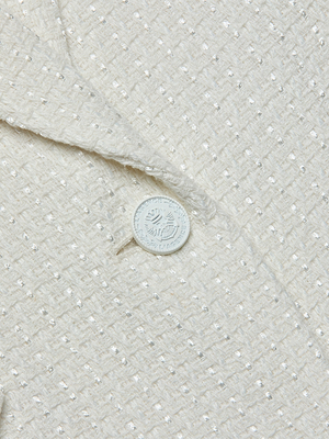 Close-up of the Jennah Tweed Blazer’s textured ivory fabric, featuring a subtle checkered pattern, single white button, and decorative lapel edge.