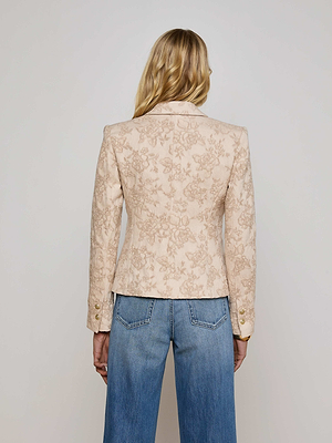 A person with long blonde hair is seen from behind, wearing the L'AGENCE Sale Jennah Jacquard Blazer in light beige and blue jeans with visible pocket stitching, standing against a plain background.