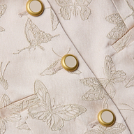 Un gros plan du haut blazer Alice montre un tissu jacquard rose pâle avec des papillons brodés et des boutons dorés au centre crème, mettant en valeur les coutures détaillées et la texture lisse du satin.