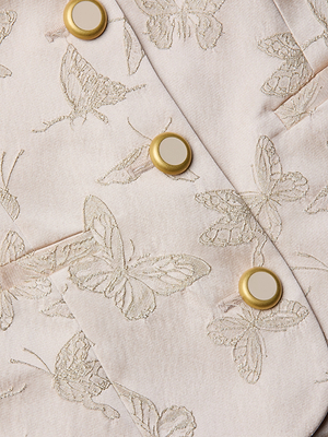 Eine Nahaufnahme des Alice Blazer Tops zeigt blassrosa Schmetterlingsjacquard mit gestickten Schmetterlingen und goldenen Knöpfen mit cremefarbener Mitte, die die detaillierten Nähte und die glatte Satinstruktur hervorheben.