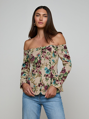 A woman with long brown hair wears the Alice Blazer Top and light blue jeans. She stands against a plain light gray background, looking confidently at the camera with a relaxed expression.