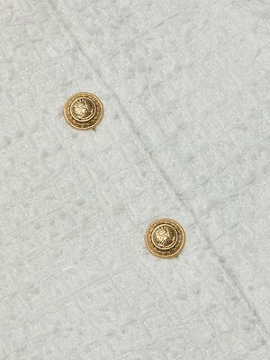Close-up of the Cove Cropped Tweed Jacket by L'AGENCE Sale, showcasing white waffle tweed with a subtle checkered pattern and two round gold embossed buttons—stylish details for a chic look.