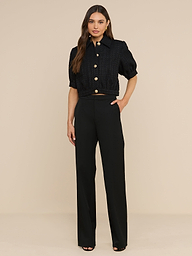 A woman stands against a plain white background, wearing the Cove Cropped Tweed Jacket with puff sleeves and buttons, paired with high-waisted black wide-leg pants. She has long hair and one hand on her hip.
