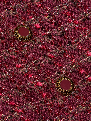 Close-up of the Cove Cropped Tweed Jacket by L'AGENCE, showcasing textured burgundy tweed with metallic threads and two vintage-inspired buttons framed by gold rope-like borders.
