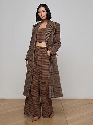 A woman with a bob haircut wears the Kolina Plaid Long Coat with matching wide-leg pants and a cropped top, standing confidently on a wooden floor against a plain light gray wall.