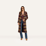 A woman wearing sunglasses, the Kolina Tweed Long Coat with a waist-cinching belt, blue jeans, and tan boots stands against a plain white background.