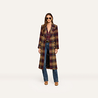 A woman wearing sunglasses and the Kolina Tweed Long Coat with gold buttons, along with blue jeans and brown shoes, stands against a plain light background.