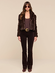 Wearing the Davy Faux Fur Jacket, brown sunglasses, a brown top, a brown belt, dark brown pants, and brown shoes, a woman stands against a plain white background.