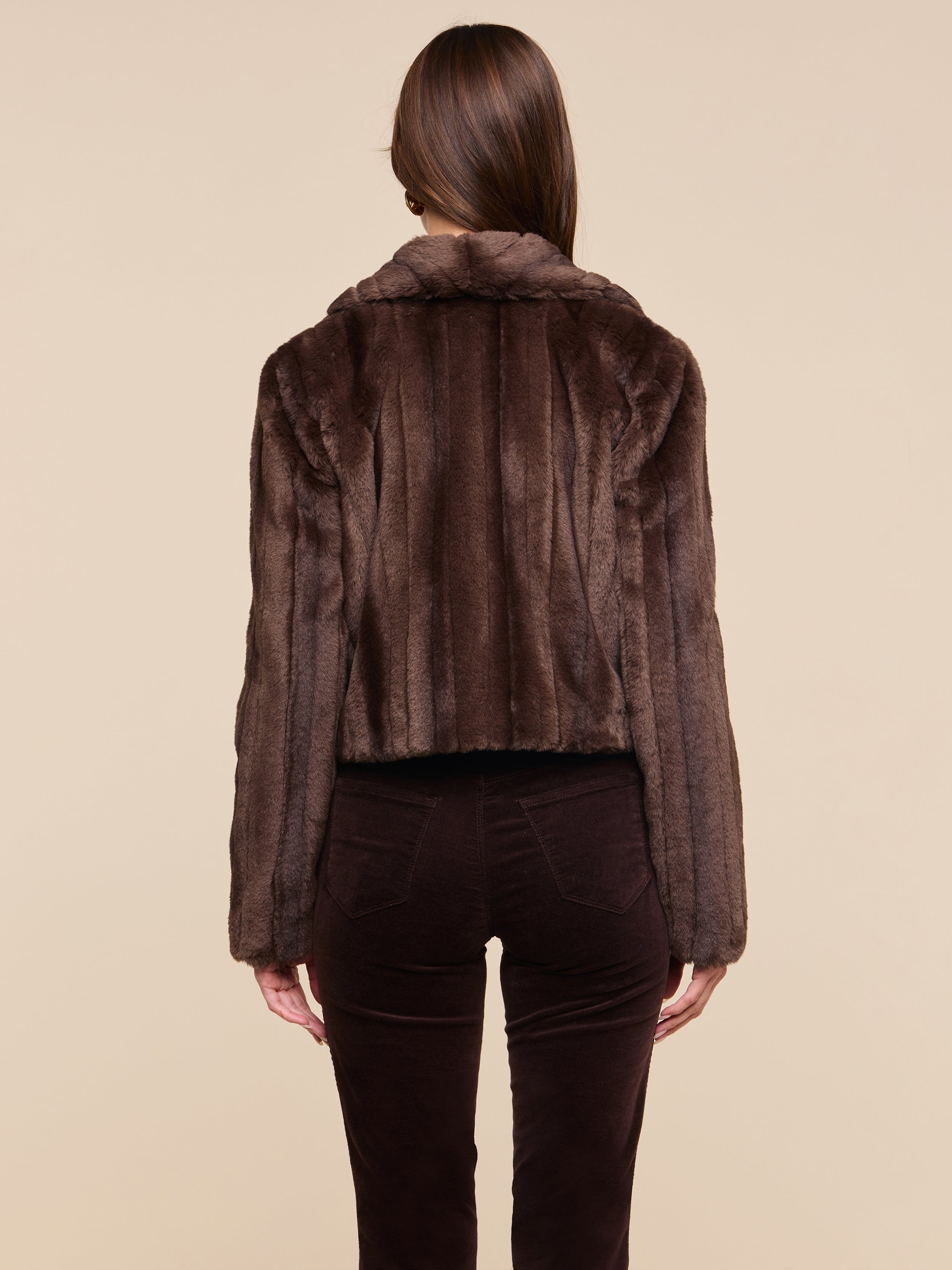 A person with straight brown hair is shown from the back, wearing the retro-inspired Davy Faux Fur Jacket and dark brown pants against a plain light background.