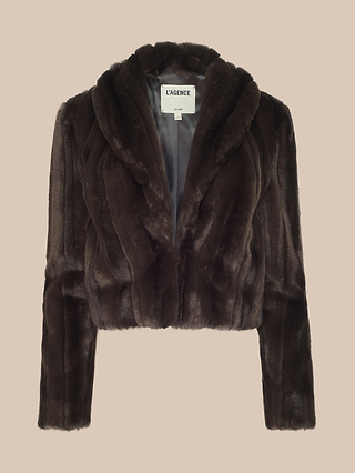 A dark brown Davy Faux Fur Jacket featuring a retro-inspired, cropped silhouette with long sleeves and a wide shawl-style collar is displayed on a beige background. The label inside reads LAGENCE.