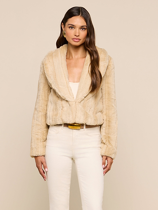 A woman wearing the Davy Faux Fur Jacket in light beige over a white top and cream pants stands against a plain beige background, looking at the camera with a neutral expression.