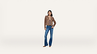 A woman stands against a plain white background, wearing a brown jacket, a light top, blue flared jeans, and brown shoes, with one hand on her hip.