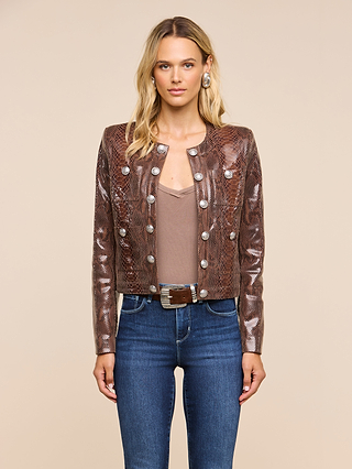 A woman with long blonde hair wears the Jayde Leather Jacket—a brown snake print style with silver buttons—paired with a taupe top, blue jeans, and a wide belt, standing against a plain beige background.