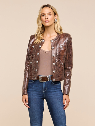 A woman wearing the Jayde Leather Jacket, featuring a brown snake print with silver buttons, pairs it with a taupe top, blue jeans, a belt, and large earrings as she stands against a beige background.
