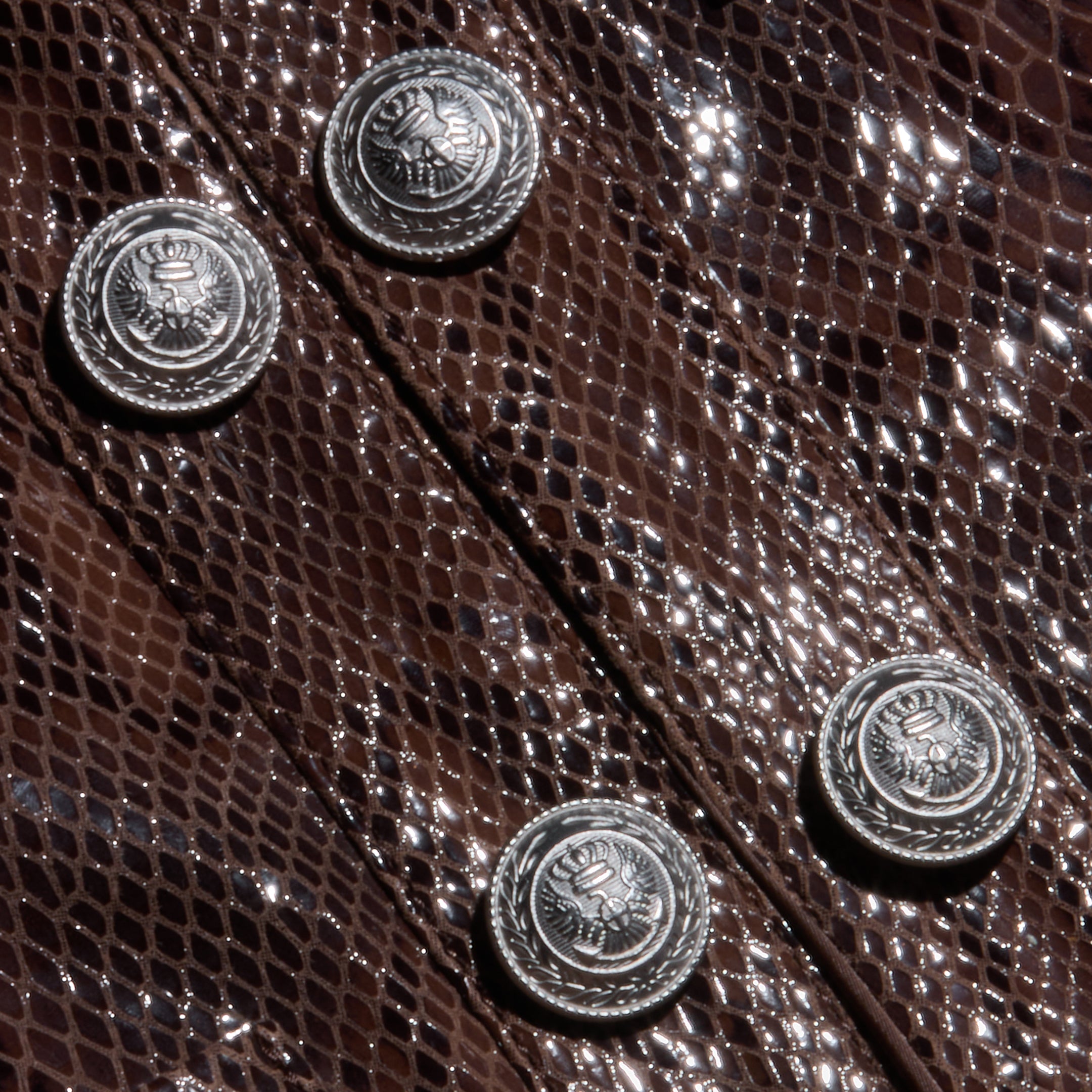 Close-up of the Jayde Coated Suede Jacket in a shiny, dark brown snake print, detailed with four silver buttons featuring crown and crest emblems.