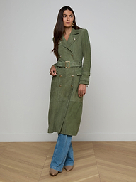 A woman models the Celina Suede Trench Coat in olive green, styled over blue jeans and beige shoes, standing against a plain white background.