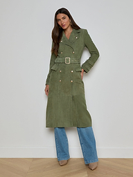 Woman wearing a long olive green Celina Suede Trench Coat over blue jeans and tan heeled shoes, standing against a plain white background—a perfect addition to any timeless wardrobe.