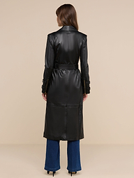 Una donna è di spalle, indossa il trench in pelle Celina nero con cintura in vita, abbinato a jeans blu scuro e tacchi neri, su uno sfondo beige a tinta unita.