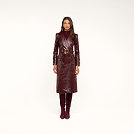 Woman wearing the Celina Trench Coat in shiny burgundy vegan leather with crocodile embossing and a matching belt, styled with a maroon turtleneck and burgundy knee-high boots, standing against a neutral background—a striking look that perfectly captures Fall 2026 fashion.