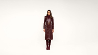 Woman stands facing forward, wearing a shiny, belted burgundy trench coat and matching knee-high boots against a plain white background.