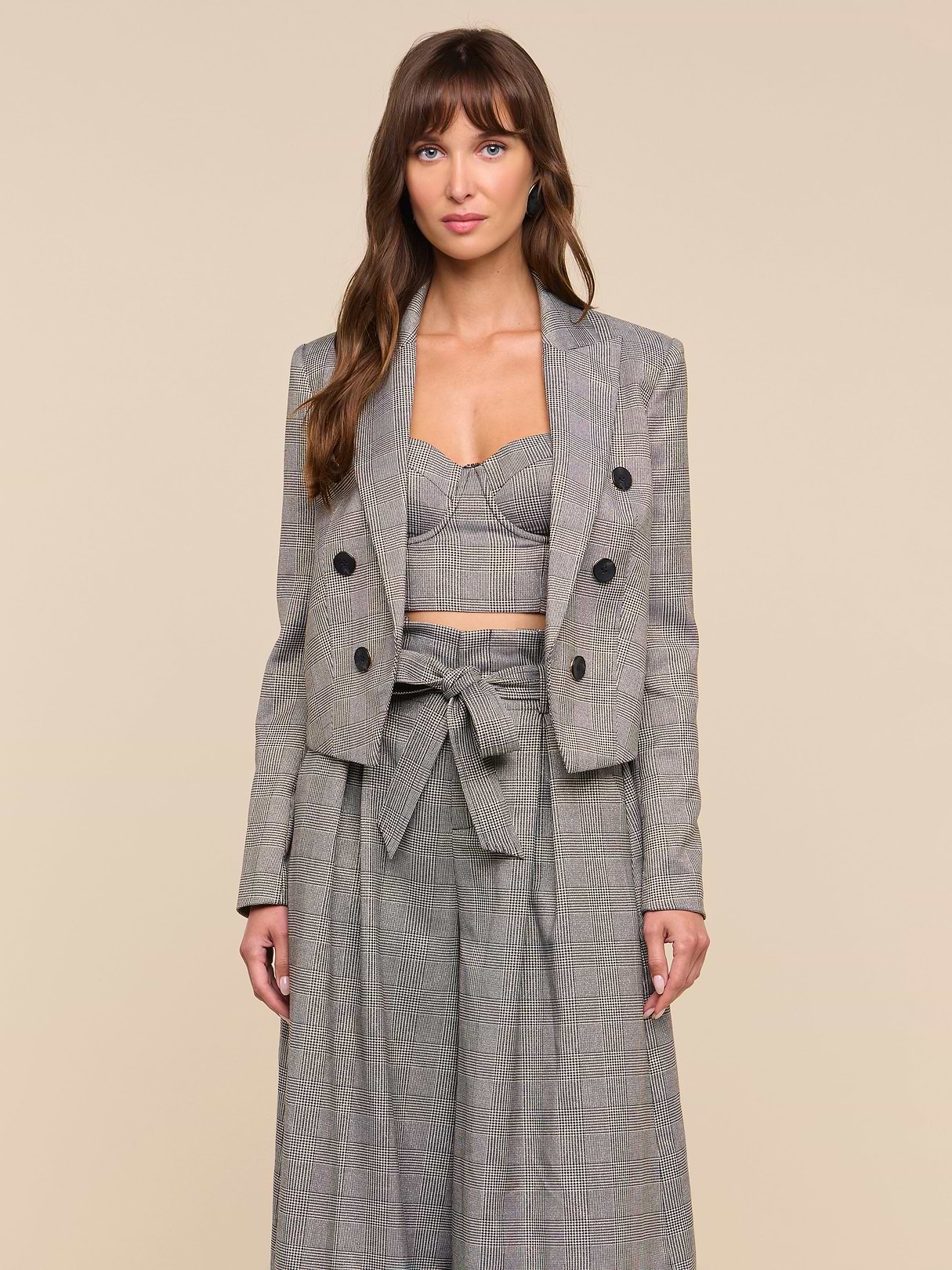 A woman stands facing forward, wearing the Lila Tweed Blazer styled with a crop top and high-waisted wide-leg pants featuring a bow tie at the waist, set against a plain light background.