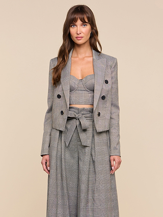 A woman wearing the Lila Tweed Blazer styled with a matching bralette and high-waisted, wide-leg trousers featuring a bow belt, standing against a beige background.