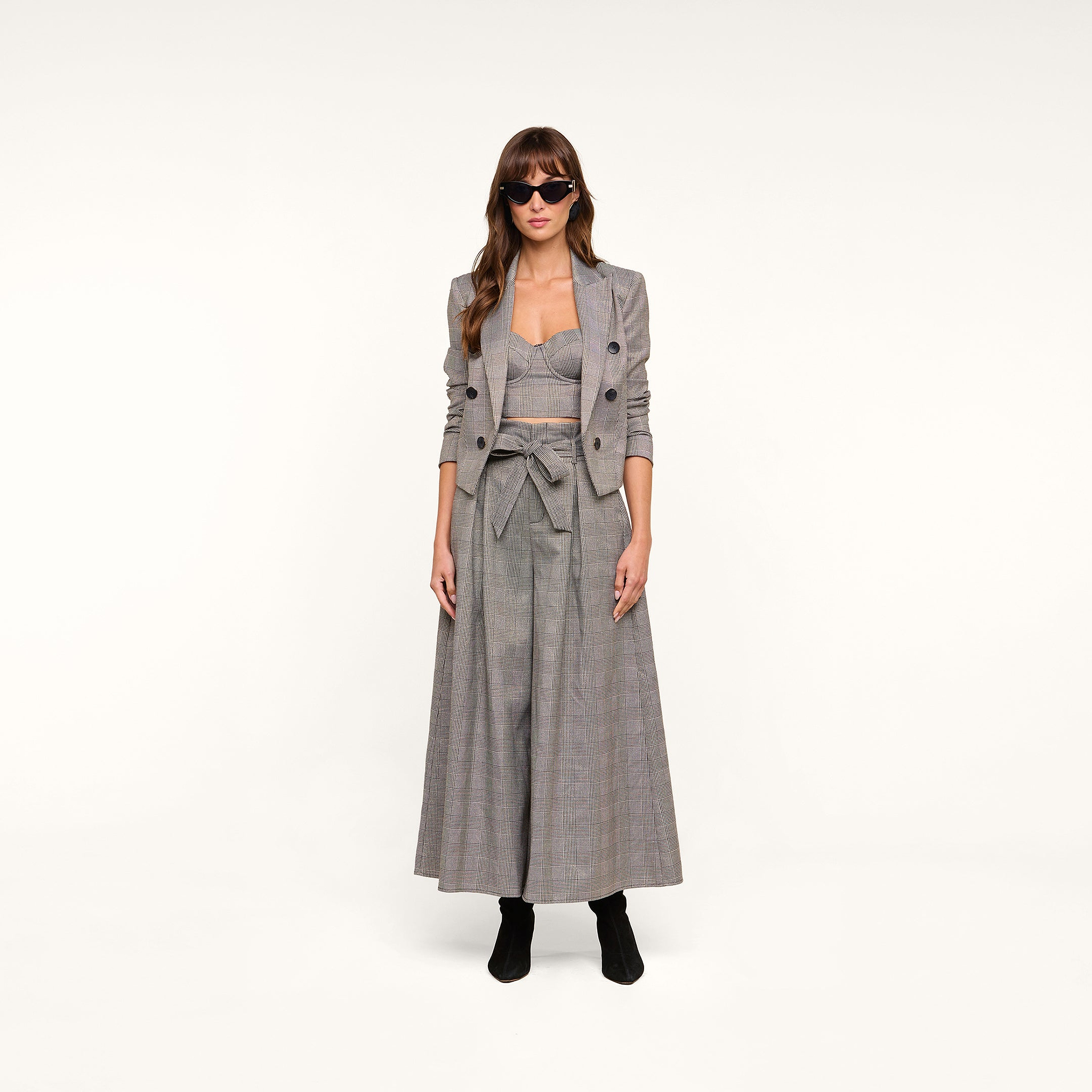 A woman wearing sunglasses, the Lila Tweed Blazer with a matching crop top and wide-leg pants, and black boots stands against a plain white background.