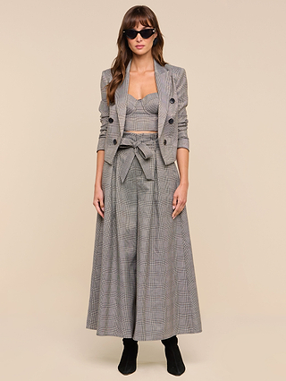 Woman wearing sunglasses, the Lila Tweed Blazer styled with matching high-waisted wide-leg pants featuring a bow belt and a coordinating bustier top, standing against a plain beige background.