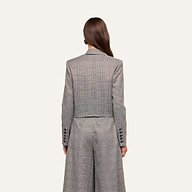 A woman with long brown hair, seen from behind, wears the Lila Tweed Blazer in a gray plaid pattern paired with matching wide-leg trousers. The background is plain and light-colored.