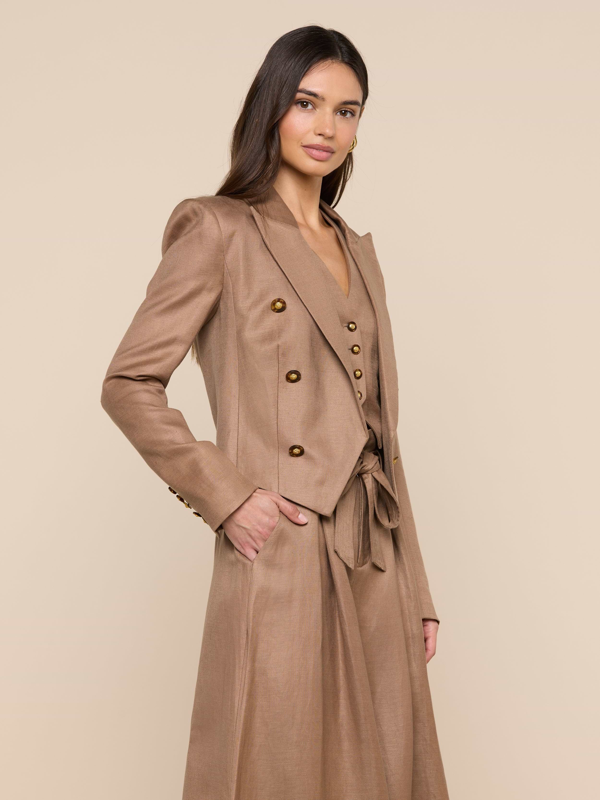Wearing the Lila Linen-Blend Blazer and a matching skirt, a woman stands with one hand in her pocket, smiling slightly against a plain light background.