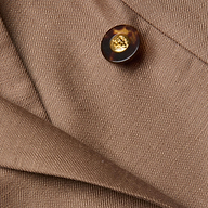 Close-up of the Lila Linen-Blend Blazer in brown, showcasing a tortoiseshell button with a gold center and overlapping fabric folds featuring a visible diagonal texture.