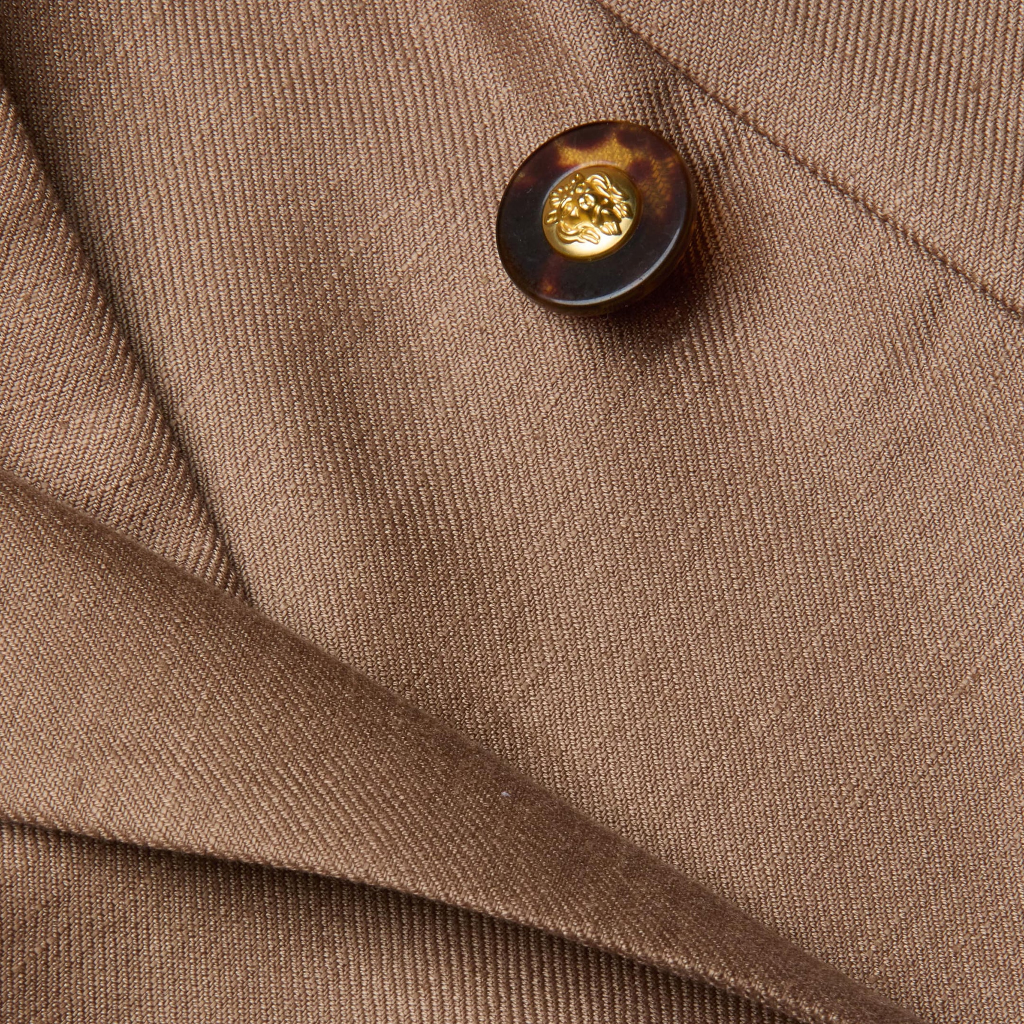 Close-up of the Lila Linen-Blend Blazer in brown, showcasing a tortoiseshell button with a gold center and overlapping fabric folds featuring a visible diagonal texture.