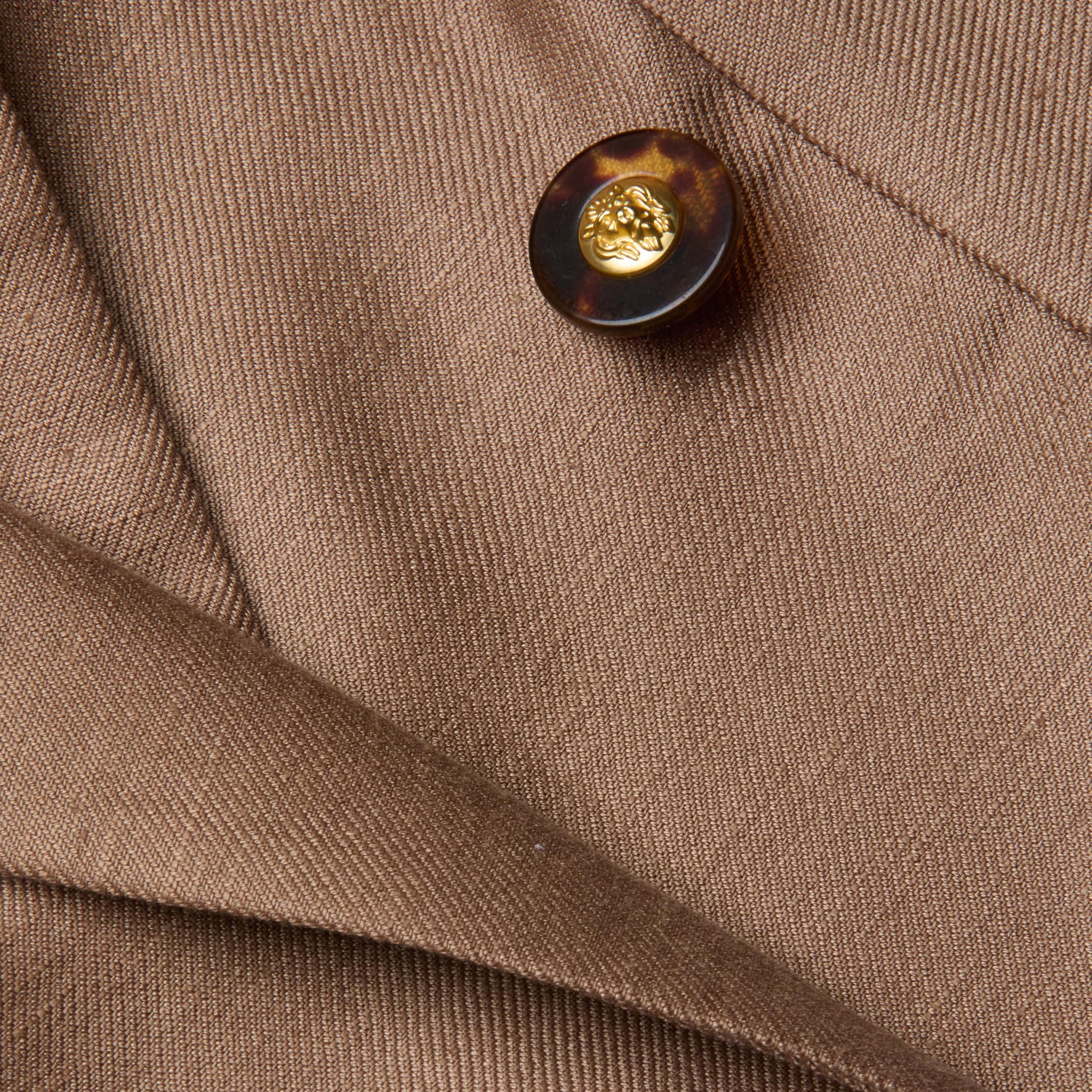 Close-up of the Lila Linen-Blend Blazer in brown, showcasing a tortoiseshell button with a gold center and overlapping fabric folds featuring a visible diagonal texture.