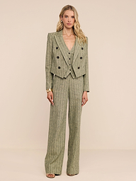 امرأة ترتدي سترة Lila Linen-Blend Blazer باللون الأخضر الزيتوني مع خطوط مخططة بالدبابيس، مع سترة مطابقة وبنطلون واسع الساقين. لديها شعر أشقر طويل وتتزين بأقراط ذهبية وسوار.