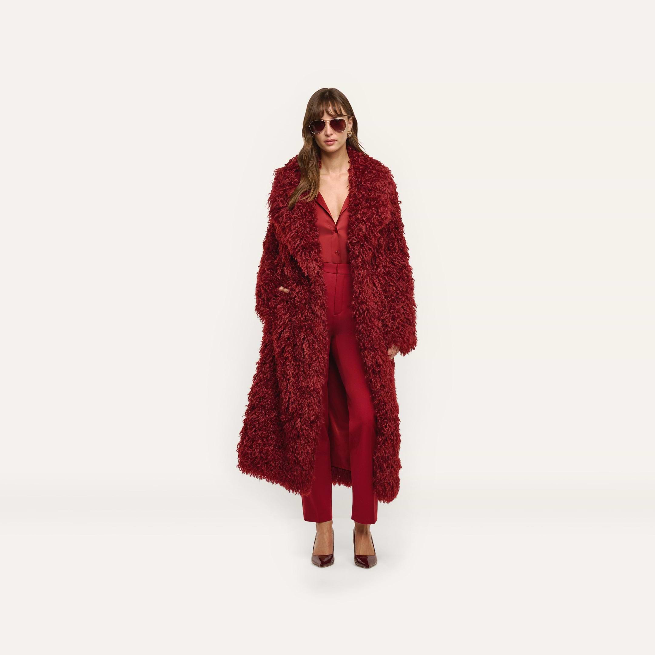 A person wearing a long, red Lizbeth Faux Fur Jacket over a matching red blouse and trousers.