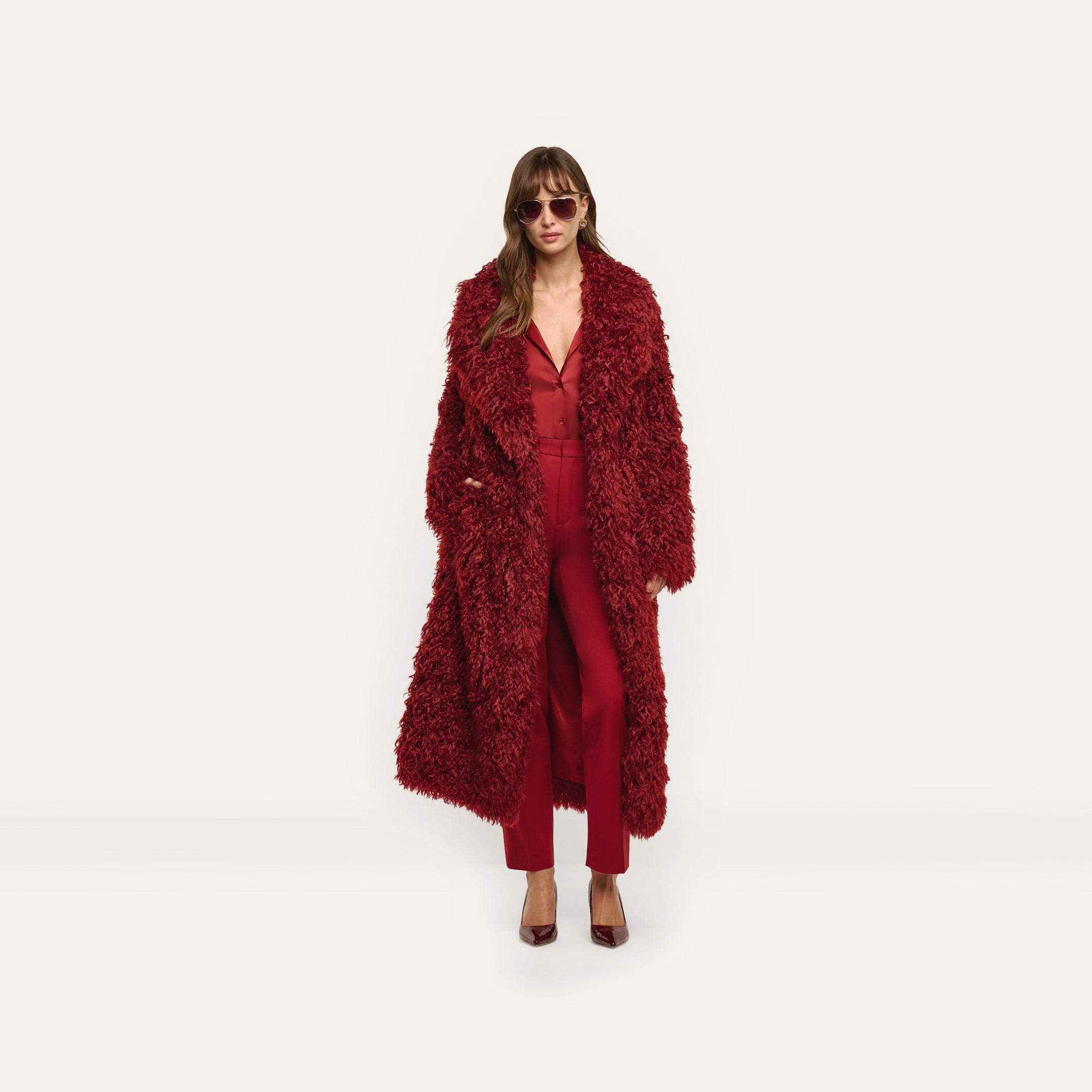 A person wearing a long, red Lizbeth Faux Fur Jacket over a matching red blouse and trousers.