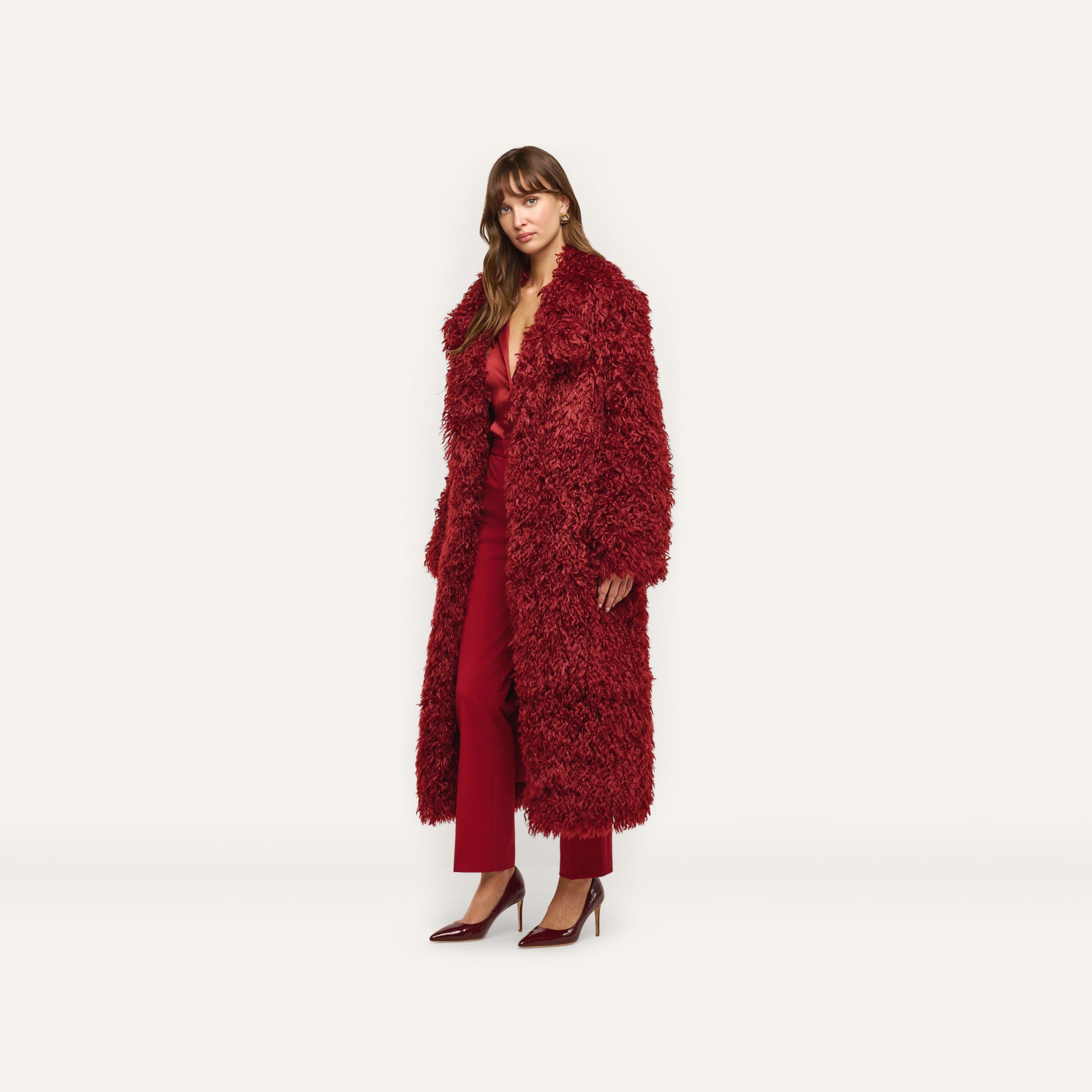 A model wears a long, deep red shag Lizbeth Faux Fur Jacket over a matching red blouse and trousers with dark red pumps.