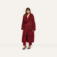 A woman wearing a deep red Lizbeth Faux Fur Jacket over matching trousers and pointed-toe heels.