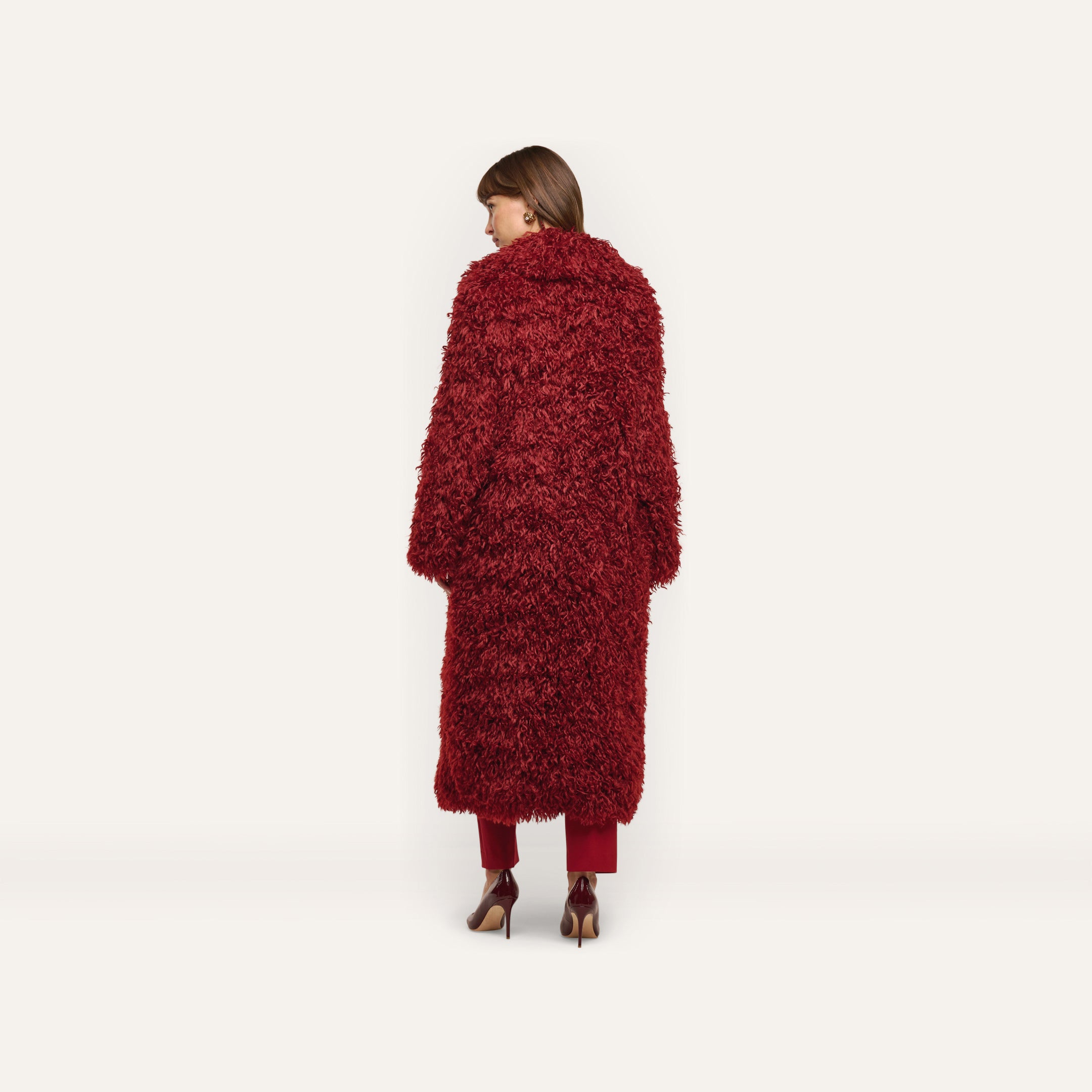 A person viewed from behind, wearing a deep red Lizbeth Faux Fur Jacket, matching trousers, and high-heeled pumps.
