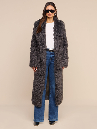 Woman wearing black sunglasses, a white top, blue wide-leg jeans, black shoes, and the Lizbeth Faux Fur Jacket in dark gray stands against a beige background—a look reminiscent of relaxed fit jackets seen at New York Fashion Week.
