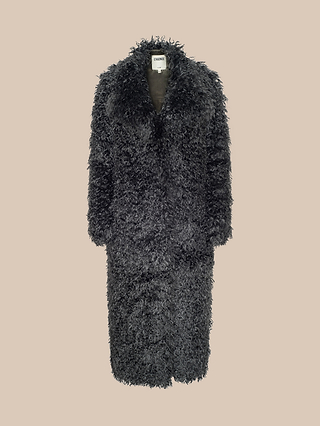 The Lizbeth Faux Fur Jacket is a long, black curly shag coat with a wide collar and full-length sleeves, showcased against a plain beige background. This relaxed-fit jacket features a textured, shaggy appearance and displays a visible white label at the neck, capturing the bold aesthetic reminiscent of New York Fashion Week.
